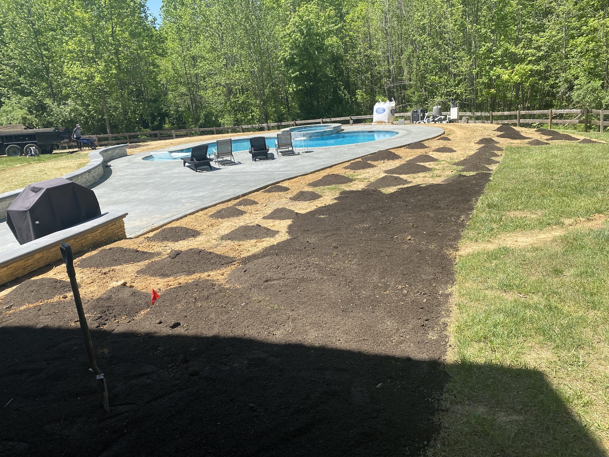 Poolside landscape bed preparation with fresh soil and mulch piles